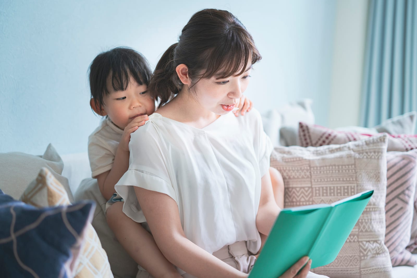 日本人の母親がソファで幼い子どもと絵本を読んでいる様子